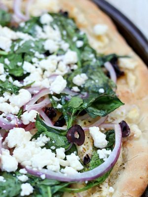 Easy Greek Pizza Recipe with a mayo & garlic spread and topped with feta, red onion, spinach, sun dried tomatoes and kalamata olives. Crazy delicious!