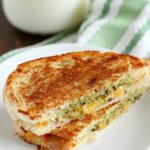 Pesto Grilled Cheese Panini cut in half on a white plate with a glass of milk in the background.