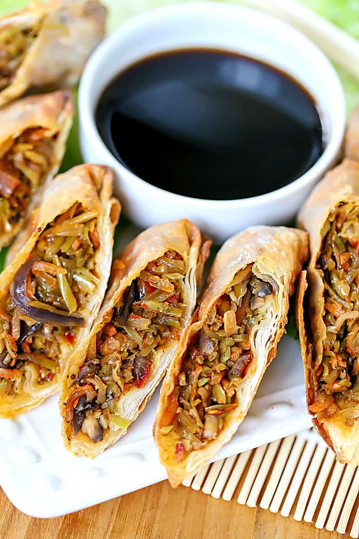 White plate with egg rolls sliced in half, surrounding a bowl of soy sauce.