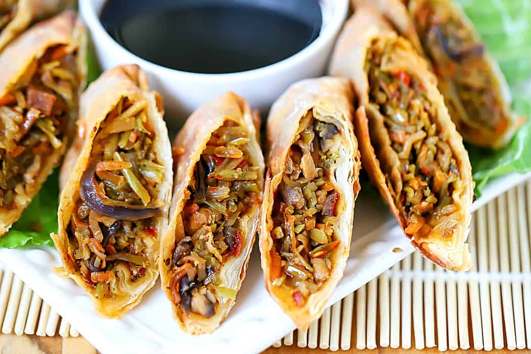 Horizontal photo of cut in half, homemade egg rolls lined up on a plate with a small bowl of soy sauce in the background.