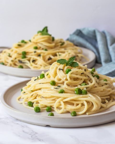 Two plates full of spaghetti pasta with a ricotta sauce and peas.