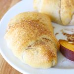 Close up of a Peach Crisp Rollup on a white plate with a side of sliced peaches.